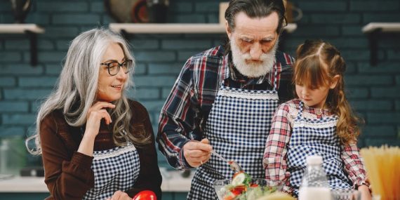 Grandparents and granddaughter preparing salad in home kitchen, creating memories together.
