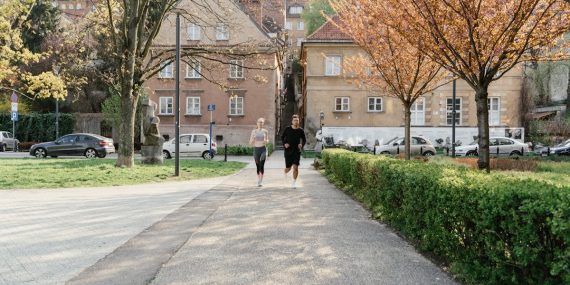 A couple jogging together in an urban park surrounded by greenery and houses.